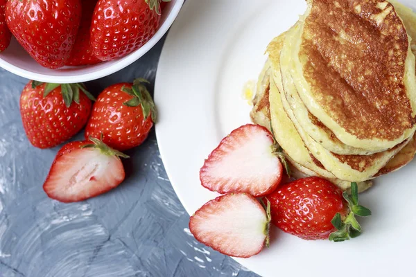 Pfannkuchen auf einem Teller und Erdbeeren auf grauem Hintergrund — Stockfoto