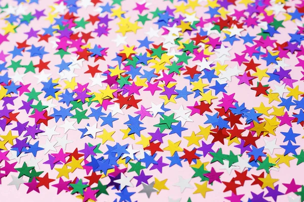 Multicolored stars of confetti on a pink background, copy space