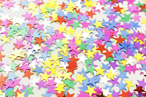Multicolored stars of confetti on a white background, view from above