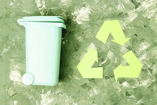 Green recycle garbage symbol and trash can on a gray background, top view.