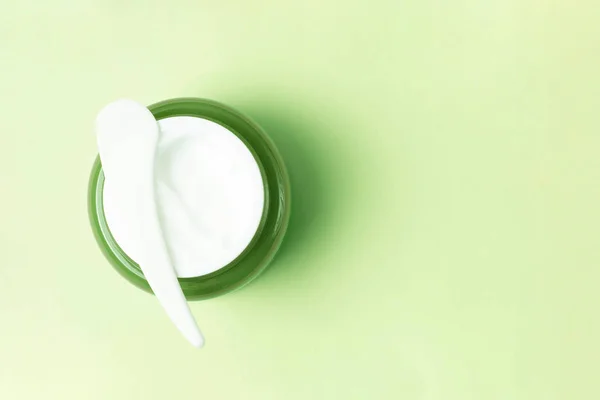 Pot vert avec crème blanche et spatule en plastique sur fond, vue du dessus, espace de copie — Photo