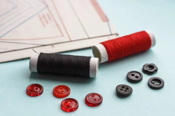 Sewing pattern, red and black threads and buttons on blue background, close-up