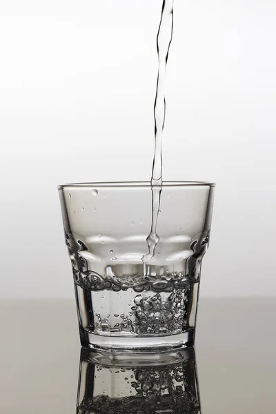 Вода наливается в стакан на светлом фоне, крупным планом — стоковое фото