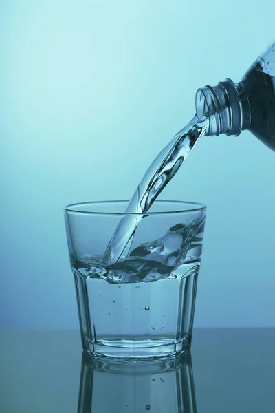 Woda jest wlewana do szklanki na niebieskim tle, zbliżenie — Zdjęcie stockowe