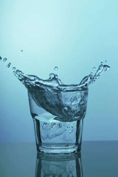 Kaca dengan air jernih dan percikan pada latar belakang biru — Stok Foto