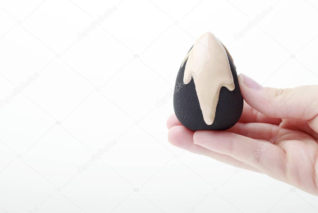 Black beauty blender with foundation in female hand on white background, copy space