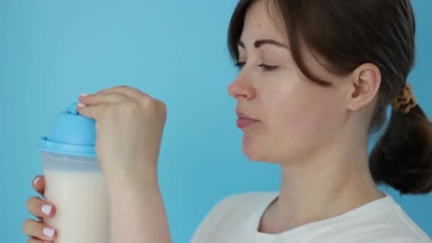 Красивая молодая девушка пьет протеиновые коктейли на синем фоне — стоковое видео