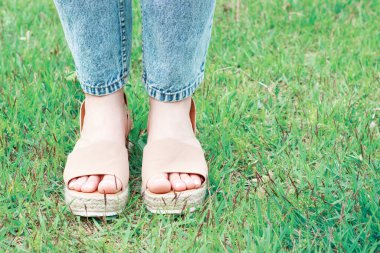 Yeşil çimenlerin arka planına karşı yaz ayağında kahverengi sandaletler, kopyalama alanı.