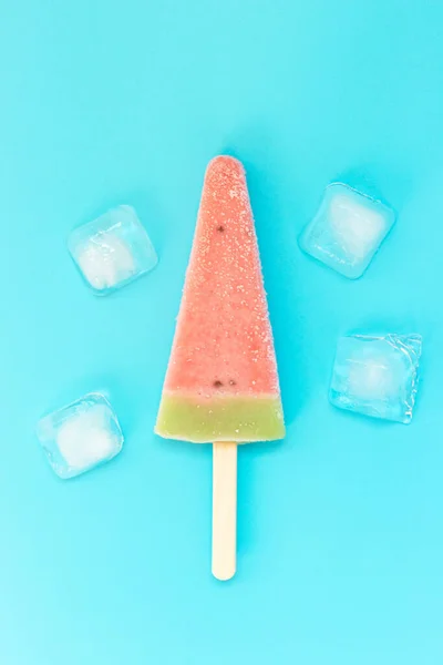Ice cream with watermelon flavor and ice cubes on a blue background, a copy of the space