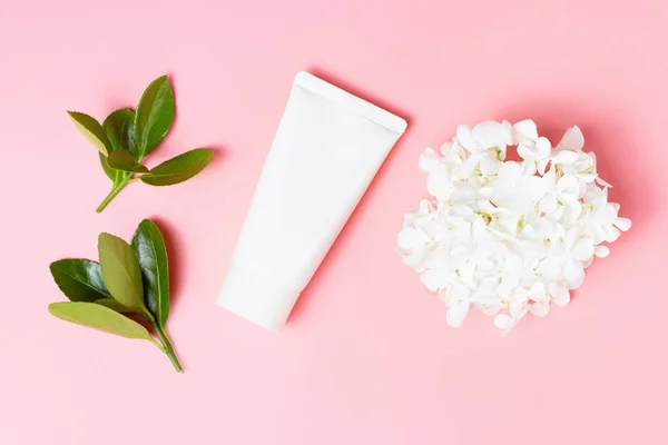 Tube blanc de crème, fleurs et feuilles vertes sur fond rose, concept de cosmétique naturelle — Photo