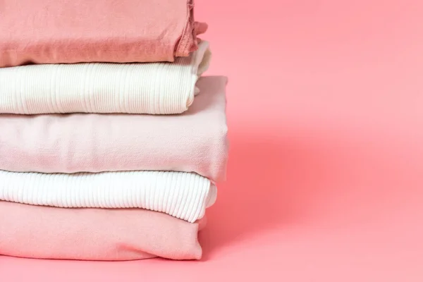 Clothes of different colors are folded neatly into stack on a pink background