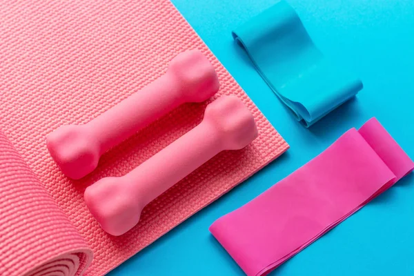 Sports accessories and yoga mat on a blue background top view.