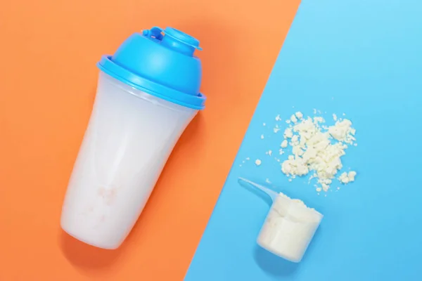 Protein shake and measuring spoon with powdered protein on a blue and orange background, a copy of the space