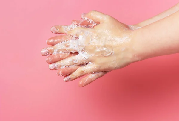 The girl washes her hands with soap and foam on a pink background