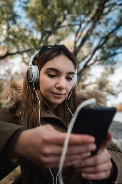 Kafkasyalı bir kadının kulaklık takıp parkta akıllı telefonuyla mesajlaşmasını kapat.