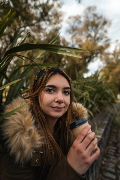 Parkta dinlenirken ve kahve içerken kameraya gülümseyen güzel bir kadın. Dikey