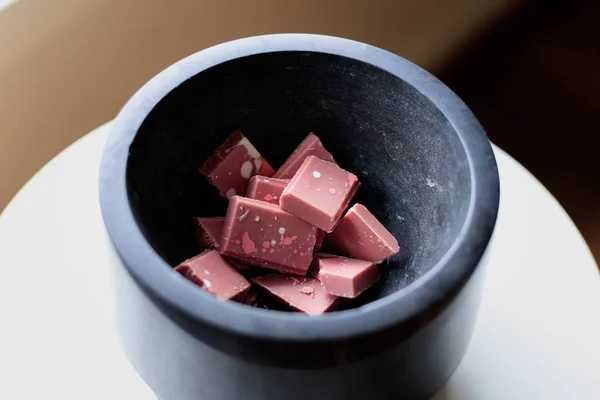 Broken and shattered pieces of ruby red chocolate in a round charcoal stone ceramic bowl.