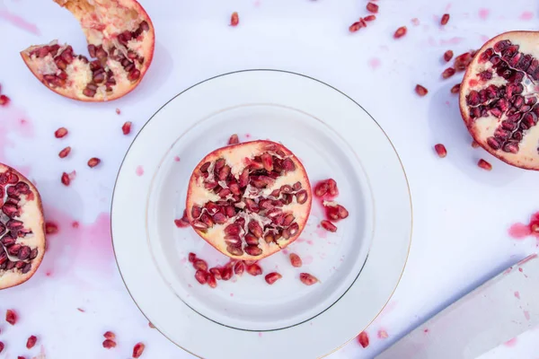 Juicy Pomegranate Fruit cut with seeds and juice on white background. Ceramic plate and knife.