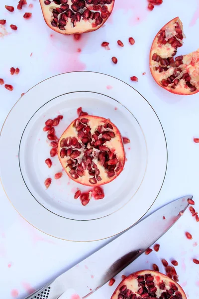 Juicy Pomegranate Fruit cut with seeds and juice on white background. Ceramic plate and knife.