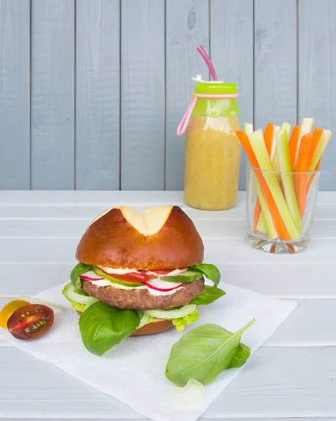 Burger s kotlet se zeleninou a zelenáč s tyčinkami celer a mrkve a bílým dřevěným pozadím — Stock fotografie