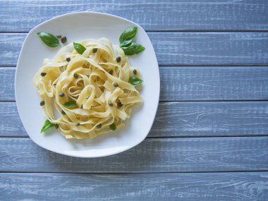 Fettuccine açık gri ahşap arka planda fesleğen ve kapanlar ile beyaz plaka üzerinde hizmet vermiştir. Seçici odak, kopya alanı