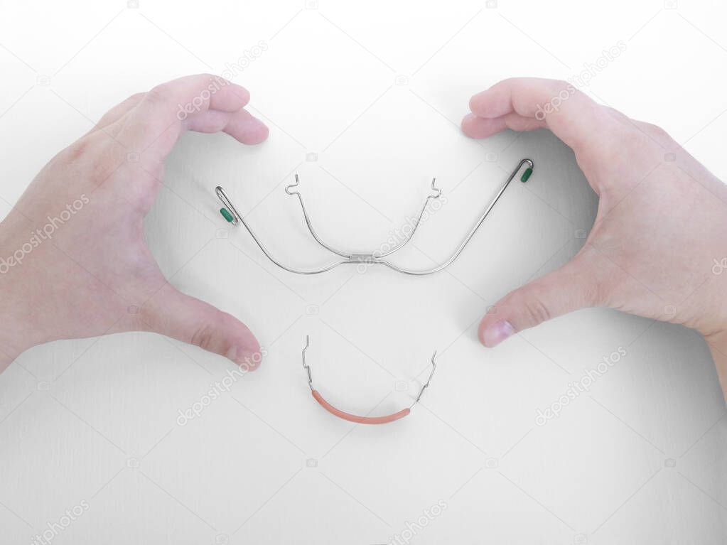 Hands on white backdrop in shape of heart around orthodontic device,removable metal braces for upper teeth,rubberized flesh-colored plastic cap for lower teeth,used with dental rubber bands.Copy space