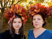 Podzimní portrét usměvavé matky a dcery s věnci utkanými z javorových listů na hlavách, proti nažloutlé přirozenosti.Koncept generační kontinuity, nedokonalosti, šťastných vztahů rodič - dítě.