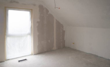 Tavan arası boş oda, Fransız penceresi, kumlu duvar kaplama için hazırlanmış gri beton zemin. Yerdeki ısıtma taşıyıcısı için uygun yer. Tavandaki kablolar üstten aydınlatma için. Boşluğu kopyala..