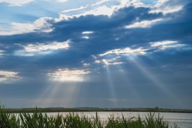 Nehri üzerinde dramatik güneş ışınları ile bulutlu gökyüzü.