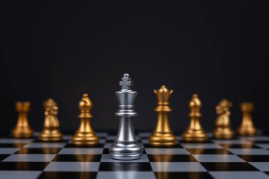 White chess king surrounded by black pieces on chess board.