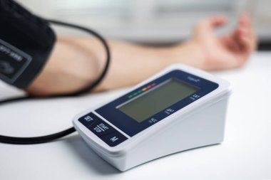 Eller masanın üzerinde bir tonometre ile. Gömlekli bir adam elektronik tonometreyle kan basıncını ölçer..