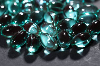 Mavi renkli yumuşak jel kapsül yığını koyu arkaplanda izole.