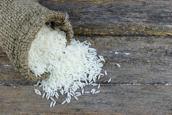 Pişmemiş Tayland yasemin pilavı, küçük kenevir çuvalına doldurulmuş, ahşap bir tahtaya dökülmüş..