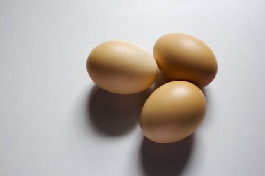 Üç yumurta beyaz zemin üzerine yerleştirilir ve siyah bir gölge var..