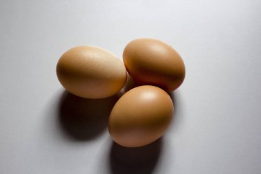 Üç yumurta beyaz zemin üzerine yerleştirilir ve siyah bir gölge var..