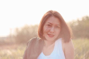 Mutlu bir gülümseme ve gün batımı ışığıyla çimen tarlasında oturan bir kadın