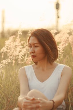 Mutlu bir gülümseme ve gün batımı ışığıyla çimen tarlasında oturan bir kadın