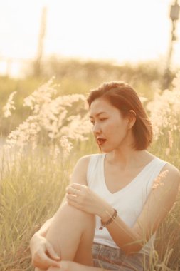 Mutlu bir gülümseme ve gün batımı ışığıyla çimen tarlasında oturan bir kadın