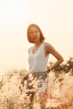 Çimlerin üzerinde mutlu bir gülümseme ve gün batımı ışığıyla duran bir kadın.