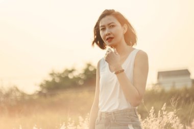 Çimlerin üzerinde mutlu bir gülümseme ve gün batımı ışığıyla duran bir kadın.