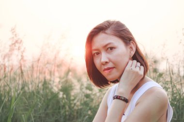 Çim tarlasında oturan kadın. Arka plan günbatımı ışığı.