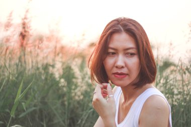 Çim tarlasında oturan kadın. Arka plan günbatımı ışığı.