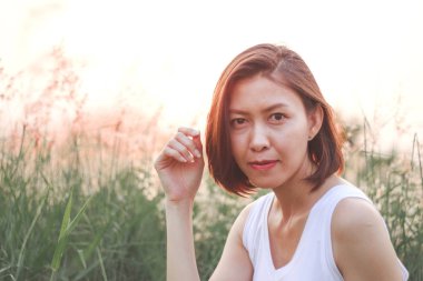 Çim tarlasında oturan kadın. Arka plan günbatımı ışığı.