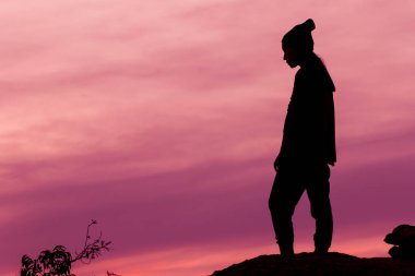 Gün batımı ışığı olan bir kayanın üzerinde duran kadın silueti.