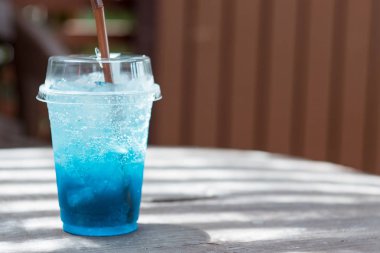 Ahşap bir masaya yerleştirilen plastik cam mavi soda