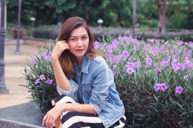 Çiçeklerin güzel çiçek açtığı bir parkta oturan kadın.