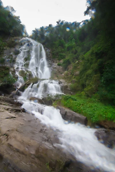 A natural waterfall flows down a long line from a cliff into a sprinkling valley.