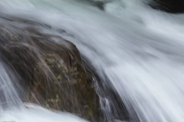 A natural waterfall flows down a long line from a cliff into a sprinkling valley.