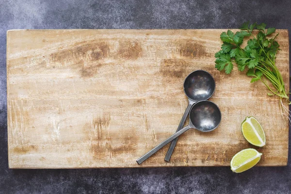 Holz Schneidebrett Hintergrund Zwei Küchenlöffel Limettenscheiben Und Korianderkräuter Auf Dunklem — Stockfoto