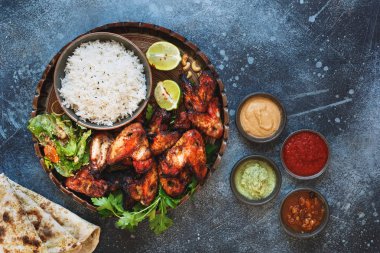 Tandoori kanatları ile pilav pirinç, yumuşak sarımsak peynir naan soslar daldırma farklı Hint turşusu ile servis tavuk. Üstten görünüm, boşluk, rustik arka plan